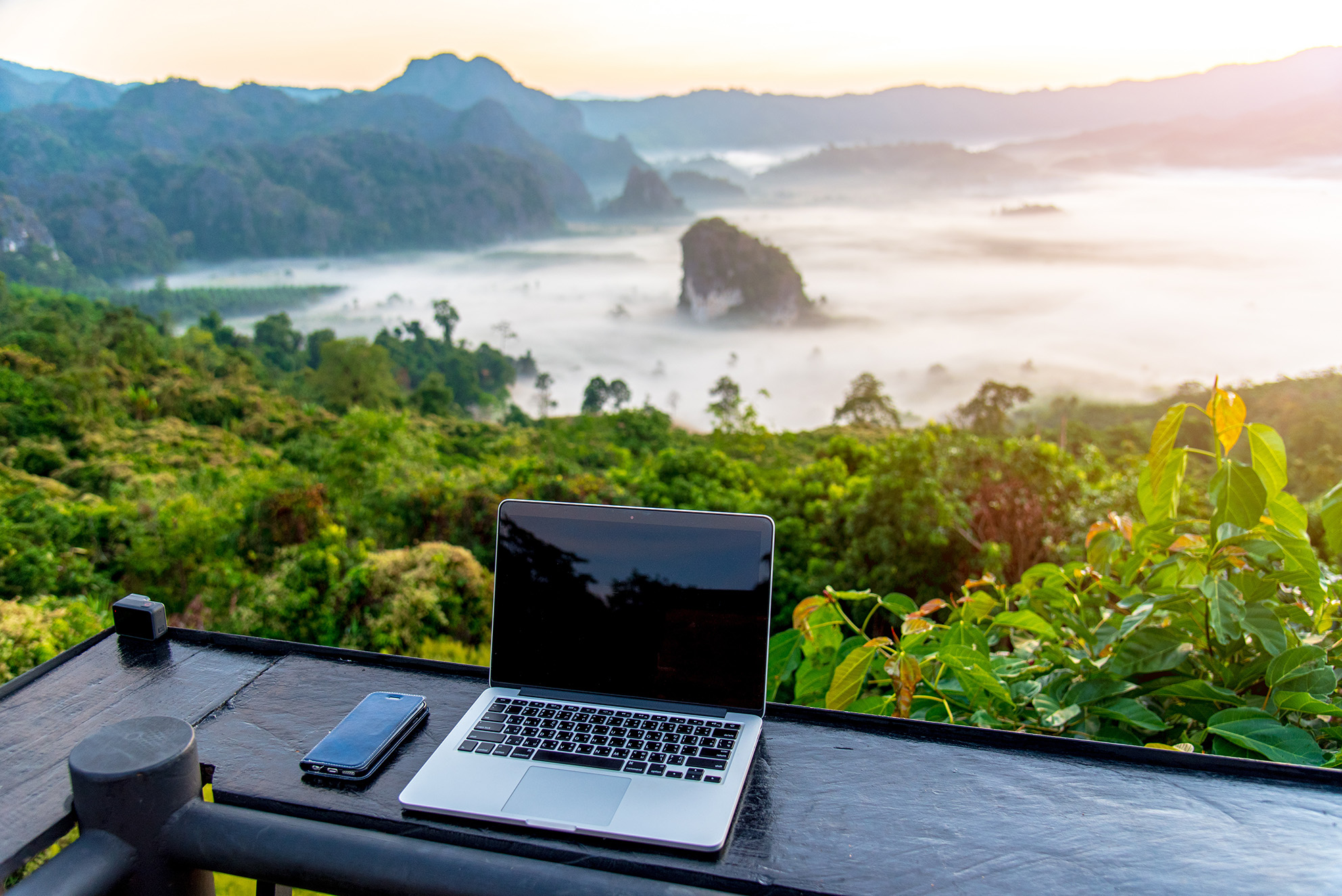 Laptop and phone on a table with a view of a mountain